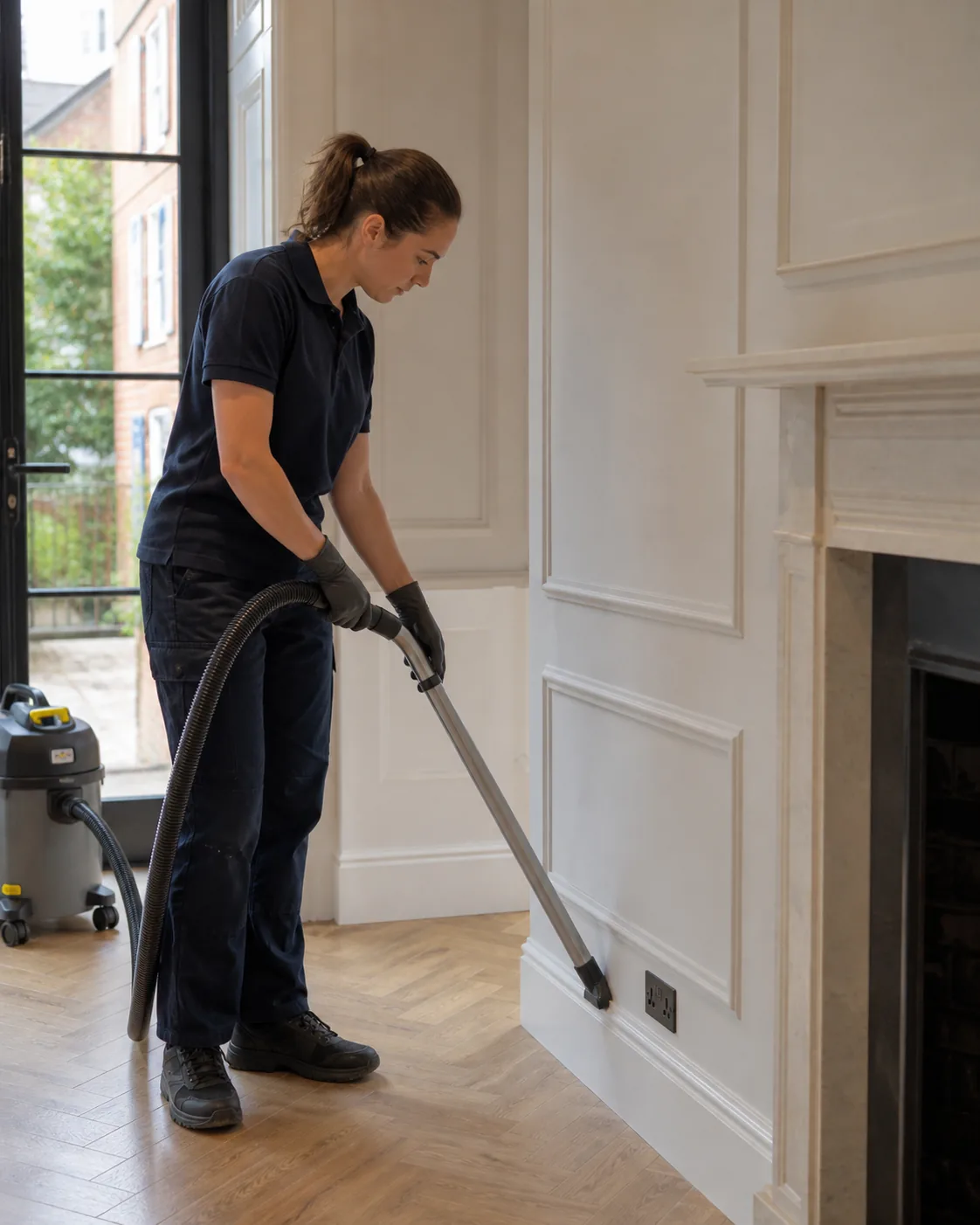 Professional cleaner removing fine renovation dust from floor edges in a London townhouse